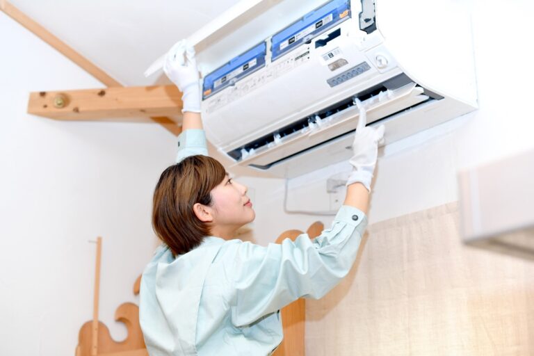 エアコンの前面パネルを開けて内部を点検する女性作業員